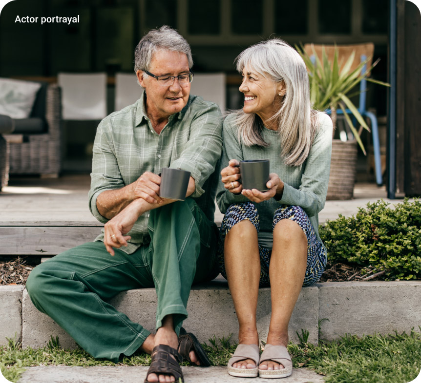 elderly couple sitting on curb holding cups