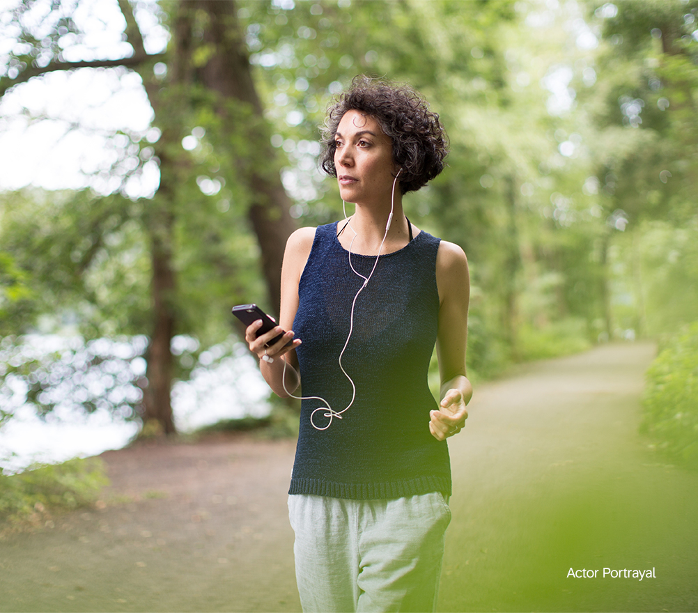 woman walking in nature with earbuds connected to phone